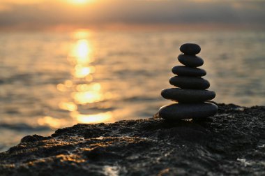 Pürüzsüz, karanlık taşlardan oluşan dikkatli bir düzenleme, gün batımında sakin okyanus sularından yansıyan, kayalık bir yüzeyde bulunur..