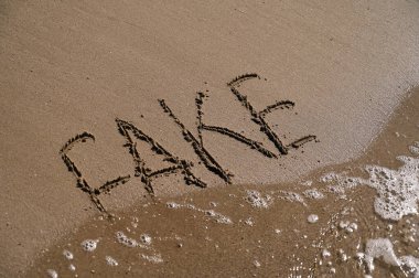 In the warm glow of daylight, the word FAKE is inscribed in the soft sand by the ocean, gently kissed by the waves. The scene invites reflection on authenticity. clipart