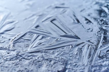 Karmaşık buz oluşumları sabahın erken saatlerinde titreşiyor, keskin açılar ve donmuş bir pencerenin yüzeyinde kışın arka planına karşı kristal güzellikler sergiliyor..