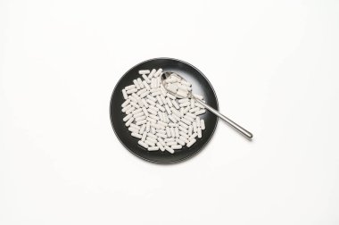 Siyah plaka beyaz kapsüller içerir, yanına bir kaşık yerleştirilir, temiz bir görünüm yaratır..