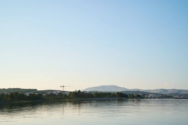 Sakin göl suyu bulutsuz gökyüzünü yansıtırken bir vinç uzak tepelerin üzerinden gündüz boyunca uzanıyor..