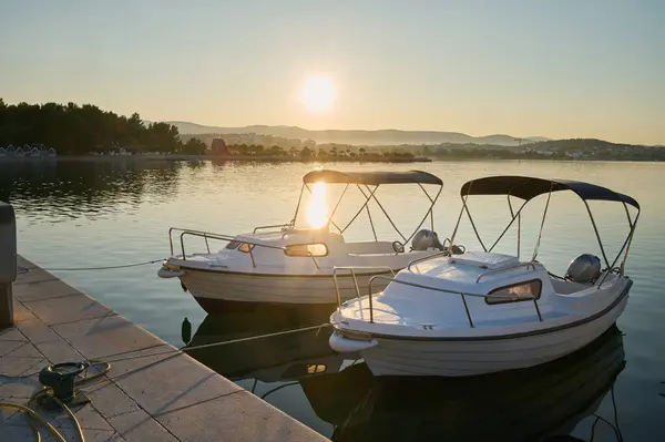 Güneş doğarken iki motorlu tekne durgun su tarafından demirlenir ve huzurlu bir sabah atmosferi yaratır..