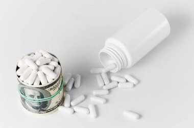 Bir bant ile çevrili para yığınları bir hap kutusunun yanında oturuyor, beyaz haplar yüzeye saçılmış..