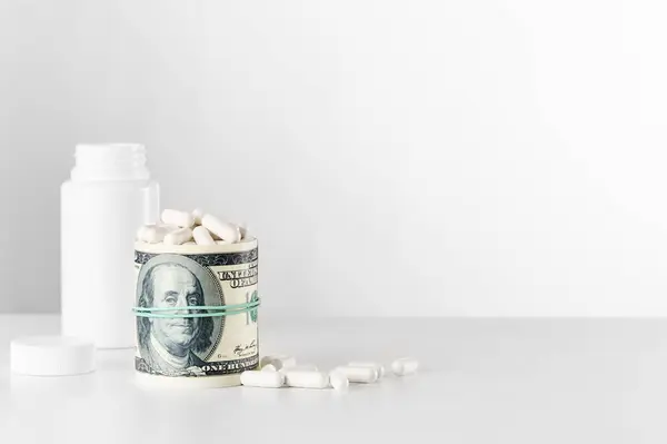 Bir tomar para bir bantla sarılmış ve bir şişeden dökülen beyaz haplarla çevrelenmiş..