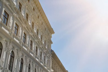 Tarihi bir bina, güneşli bir günde parlak mavi gökyüzüne karşı mimari özellikler sergiliyor..