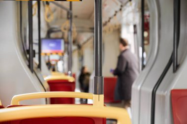 Bir yolcu, sakin bir gündüz seferi sırasında boş koltuk ve tırabzanlarla çevrili modern bir tramvayda duruyor..