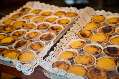 Sıcak bir pastanede dantelli tepsilerde sergilenen taze kremalı tartlar..