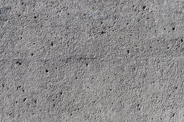 Yakından bakıldığında, beton bir duvarın pürüzlü ve düzensiz dokusunu ve küçük girintileri gösterir.