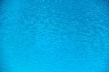 Sakin bir sahil ortamında, öğlen güneşinin altında, su yüzeyinde hafif dalgalar dalgalanır..