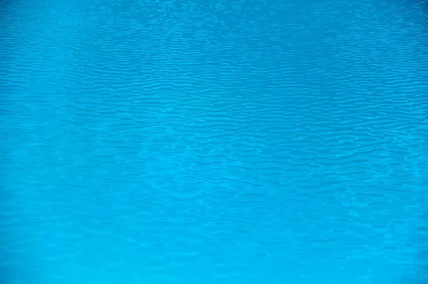 Sakin bir sahil ortamında, öğlen güneşinin altında, su yüzeyinde hafif dalgalar dalgalanır..