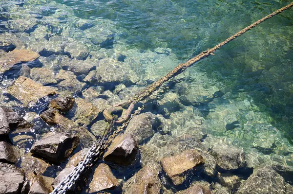 Sudaki kayaların üzerine uzanan ağır bir zincir sakin turkuaz sularda sahnenin doğal güzelliğini vurgular..