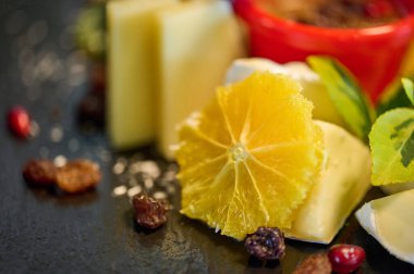 Koyu bir tabakta çeşitli meyve ve peynir çeşitleri, canlı renkler ve dokular sergiliyor..