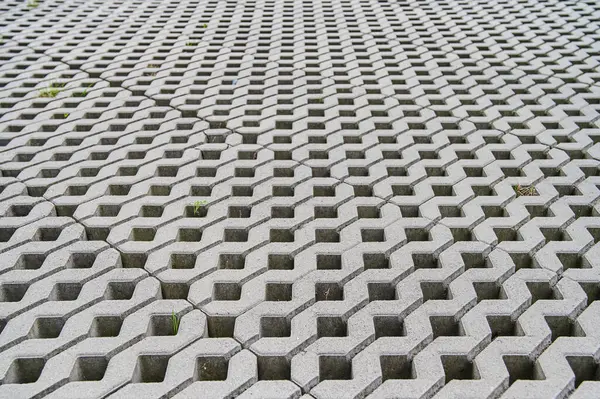 Altıgen beton blokların karmaşık örüntüsü. Güneşli bir günde, açık bir alanda çimenler çatlıyor.