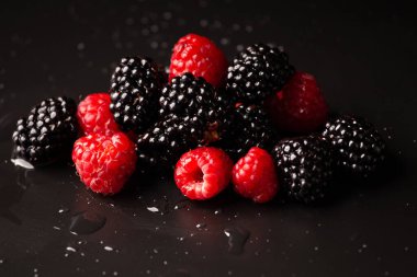 A handful of raspberries and blackberries on a black background close-up. Healthy fruits on a dark background with water drops