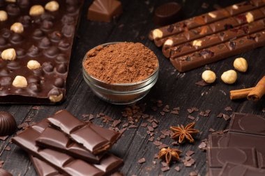 Chocolate, cocoa powder, chocolate chips, cinnamon, star anise on a dark wooden background. Handmade chocolate with nuts and spices. Composition of bars and slices of chocolate.