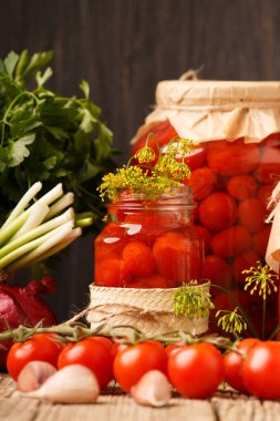 Canned tomatoes in closed jars with spices on a wooden background. Harvesting tomatoes for the winter. Canning and fresh tomatoes with garlic, pepper, dill and basil.