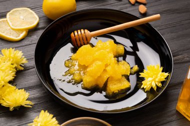 Crystallized honey, dipper in a black plate on a dark wooden background. Composition of honey, lemon, yellow flowers and petals on a black background. Useful natural products. Healthy food.