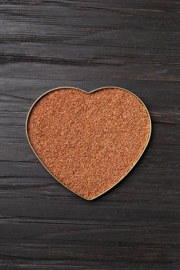 Chocolate chips are poured into a heart-shaped box on a wooden background with space for text. Milk chocolate in the shape of a heart on a dark background top view. Valentine's Day.