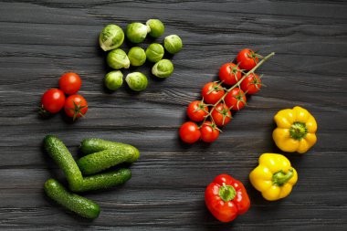 Fresh cucumbers, cherry tomatoes, colorful peppers, brussels sprouts on a dark wooden background top view. Raw vegetables. Proper nutrition. Organic products.