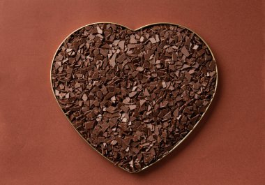 Heart shaped chocolate on brown background top view with place for text. Chocolate chips in a box in the shape of a heart on a brown background. Valentine's Day. Dark chocolate on a brown background. Love.