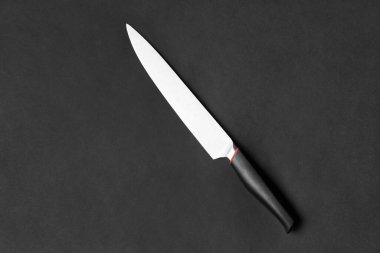 Kitchen knife with a black handle on a black background. Large knife on a dark background top view. Kitchenware. Knife with a wide blade.