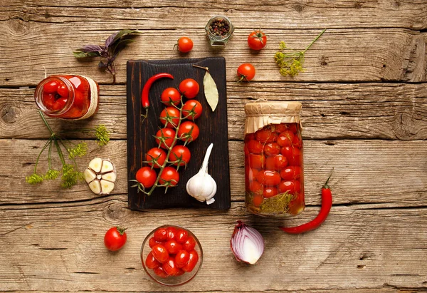 Canned tomatoes in a jar, cherry branch, garlic, chili pepper, onion on an old wooden background top view. Ingredients for marinating tomatoes. Preparation for the winter