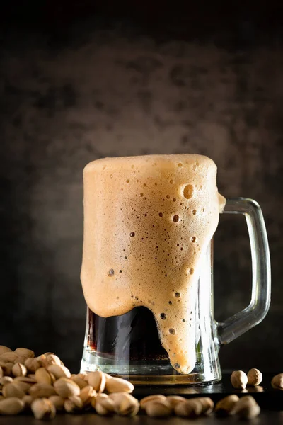 A glass of dark beer with a handful of chips on a dark background. Beer pouring from a bottle into a glass. Chips in a stack near a mug of beer with foam.