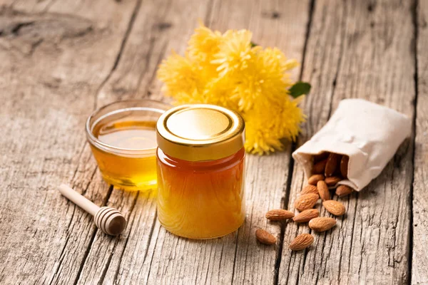 Honey in a closed glass jar and a bowl on a wooden background. Composition of honey jars, dipper, nuts in a bag, and yellow flowers. Healthy foods. organic honey. Organic products.