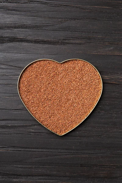 Chocolate chips are poured into a heart-shaped box on a wooden background with space for text. Milk chocolate in the shape of a heart on a dark background top view. Valentine's Day.