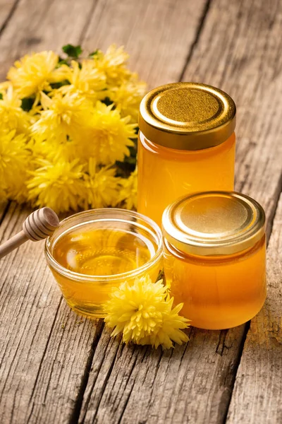 Honey in jars and plates on an aged wooden background. Composition of honey in plates of different sizes, dipper and yellow flowers. organic honey. Healthy food. Still life of honey and flowers.