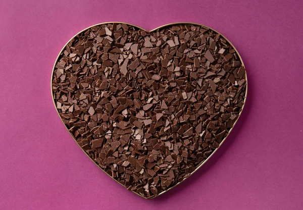 Heart shaped chocolate on a purple background top view with place for text. Chocolate chips in a box in the shape of a heart on a purple background. Valentine\'s Day. Dark chocolate on a purple background. Love.