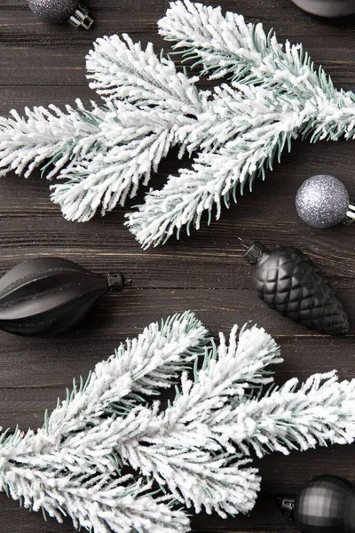New Year\'s decor on a dark background with a place top view. Fir branch in the snow and Christmas decorations in black on a wooden background. Christmas composition on a dark background.