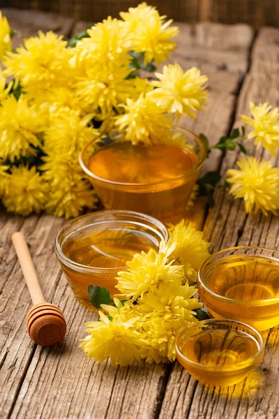 Composition of honey in bowls of different sizes, wooden dipper and yellow flowers on an aged wooden background close-up. Healthy food. Still life of honey and flowers.