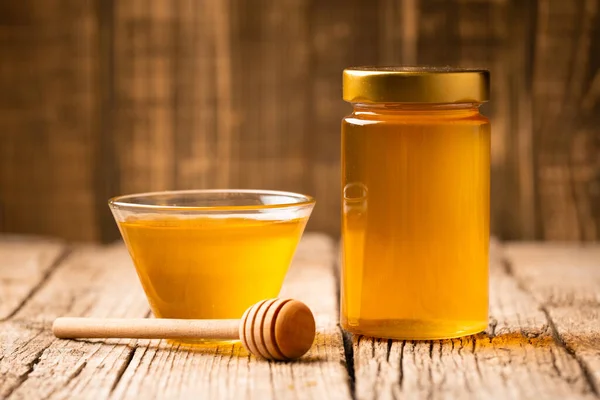 Honey in a closed glass jar and a bowl, wooden dipper on a wooden background. Composition of honey jars and spoons for honey. Healthy foods. Organic products.