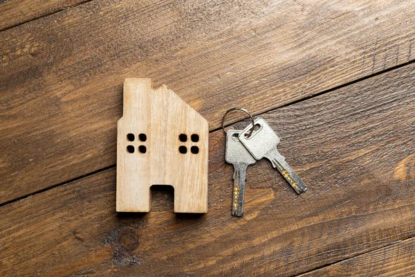 Conceptual image of a small house and keys on a wooden surface with space for text. Property For Sale. House sale advertisement. Keys to your dream house. Auction.
