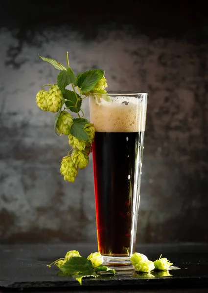 dark beer in a mug and green hop on wooden table on brown background. Oktoberfest. Beer Festival.