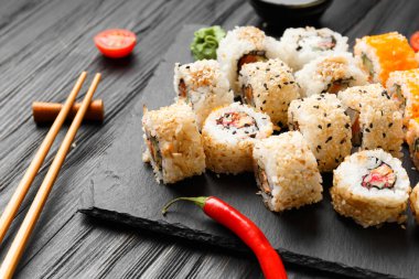 Set of salmon rolls on a dark background with chopsticks, sauce and red ginger. Red sushi with sesame on black background