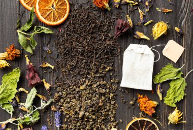 Composition of dry black and green tea, tea bag, dried citrus slices and dry hibiscus, calendula, lavender flowers on a dark wooden background top view close-up. Different types of dry tea on a dark background.