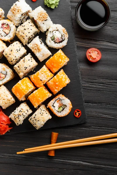 お箸やソース 紅しょうがなどの暗い背景にサーモンロールがセットになっています 黒を基調とした赤寿司 — ストック写真