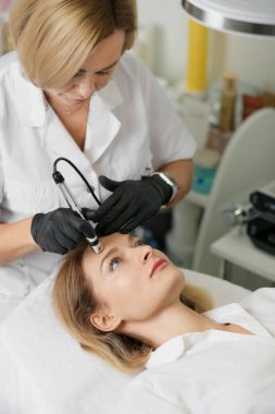 Rejuvenating facial therapy treatment at spa salon clinic. Young beautiful woman getting lifting anti-aging, face massage and skincare by electroporation facial therapy aesthetic cosmetology.