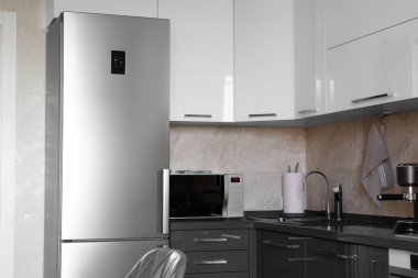 Kitchen in the apartment Design of the kitchen room. Gray kitchen interior with white cabinets. Refrigerator and microwave in stainless steel in the interior of the kitchen.