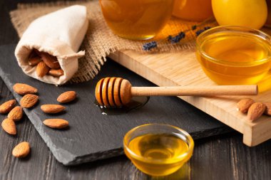 Honey in jars and a bowl, dipper, lemon, ginger, almond on a black stone plate on a wooden background. Conceptual composition of useful organic products. Natural products for the treatment of colds.