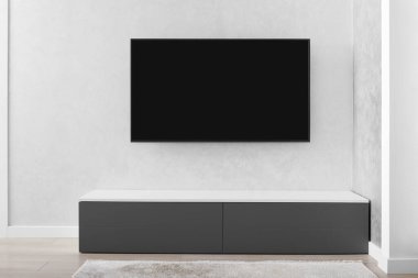 Modern bir oturma odasının bir parçası, gri bir duvarda akıllı bir LED TV, gri bir dolap, bir halı. İç mekanda minimalizm. Hafif tonlu oturma odaları.