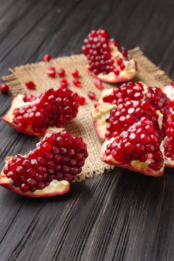 Kırık olgun nar, büyük taneler, dağınık tohumlar bir çuval bezi üzerinde ve yakın plan koyu ahşap bir arka plan. Koyu arkaplanda büyük bir narın soyulmuş parçaları..