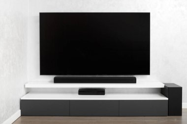 Oturma odasının içinde duvarında televizyon, hifi ekipmanları, ses çubuğu, gri dolap olan bir yer. Televizyon ve müzik sistemi iç kısımda. Parlak renklerle modern oturma odası.