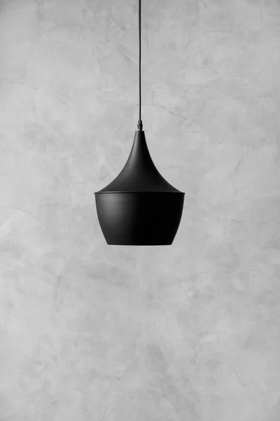 Modern loft-style black metal ceiling chandelier against a wall with decorative gray plaster with space for text. Black designer lamp on a gray textured background.