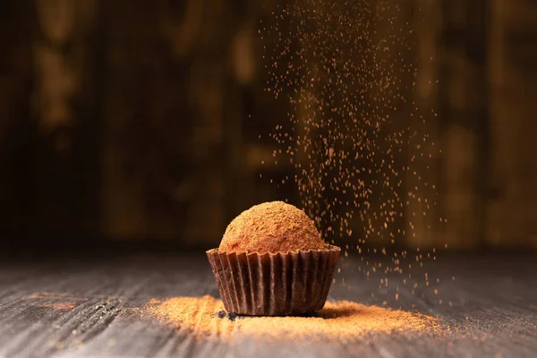 Cocoa powder is sprinkled on a chocolate truffle under a beautiful light. A ball of chocolate truffle is sprinkled with cocoa on a dark background close-up. Conceptual photo of a gourmet truffle.