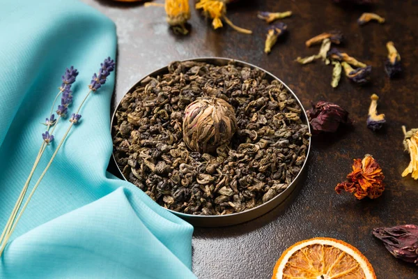 Composition of green, flower tea and dried orange slices on blue and brown backgrounds. Large-leaf tea, dried flowers and citrus chips on contrasting backgrounds.