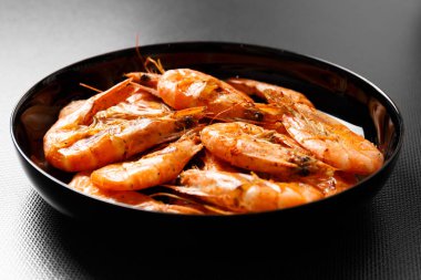 Kapalı seramik bir masada siyah bir tabakta kızarmış karides. Koyu arkaplanda karides ızgarası.