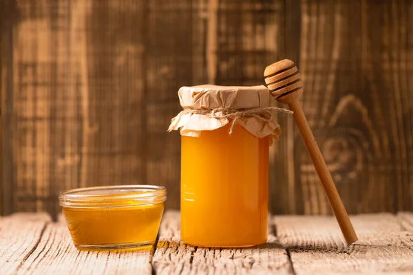 Honey in a closed glass jar and a bowl, wooden dipper on a wooden background. Composition of honey jars and spoons for honey. Organic products.
